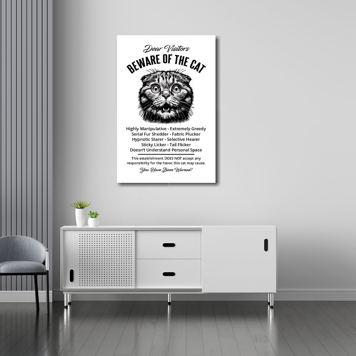 20 inch by 3 inch canvas print of a funny Scottish Fold 'Beware of the cat' notice. Mounted on a gray wall above a white sideboard.