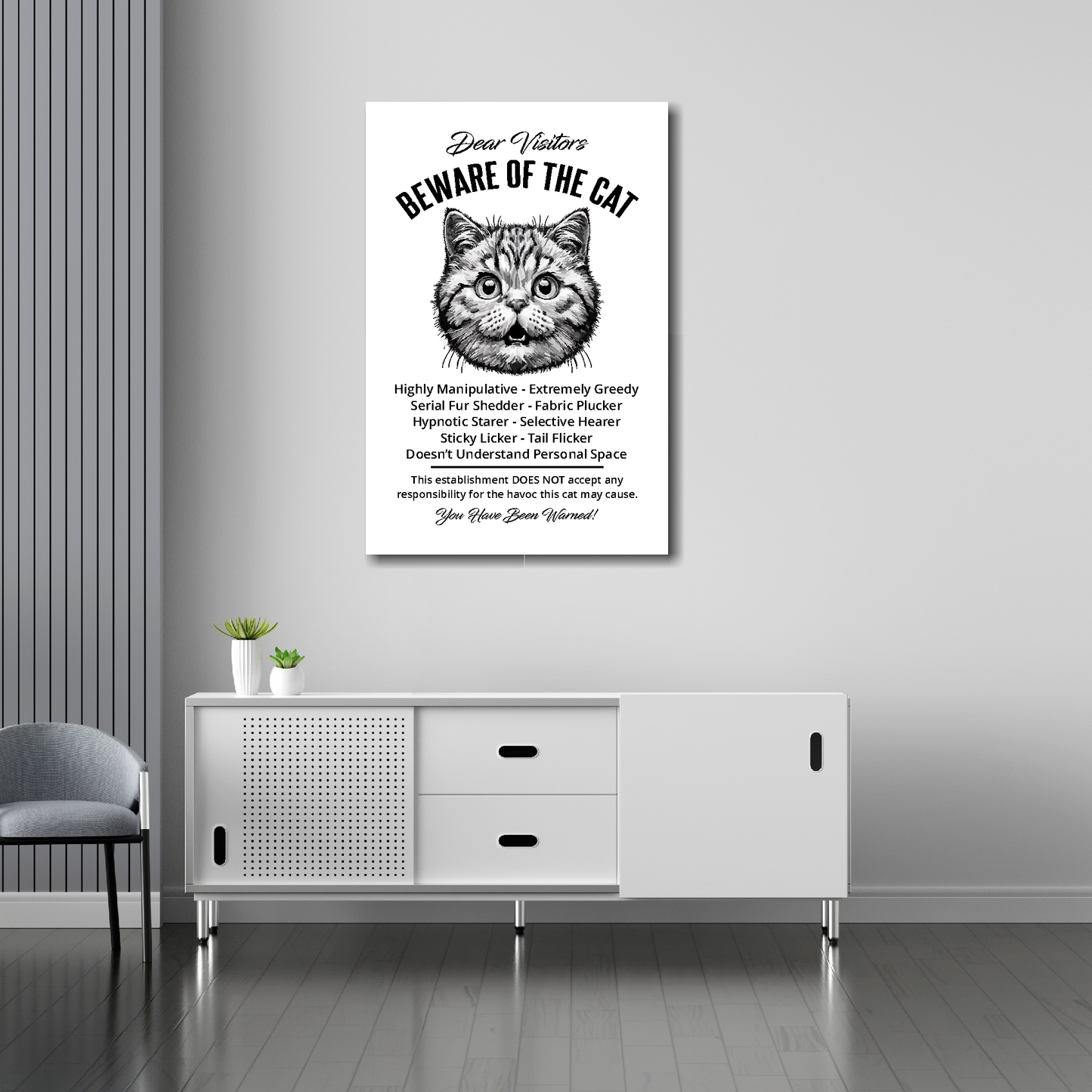 20 inch by 30 inch canvas print of a funny British Shorthair 'Beware of the cat' notice. Mounted on a gray wall above a white sideboard.