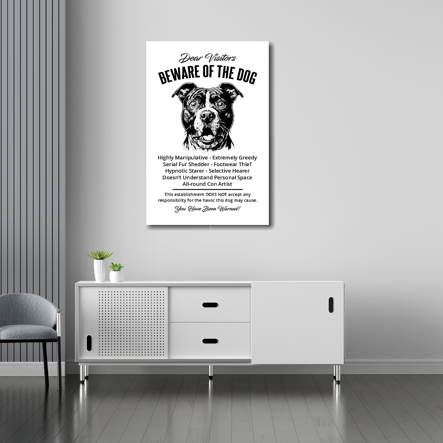 20 inch by 30 inch canvas print of a funny Staffordshire Bull Terrier 'Beware of the Dog' notice. Mounted on a gray wall above a white sideboard.