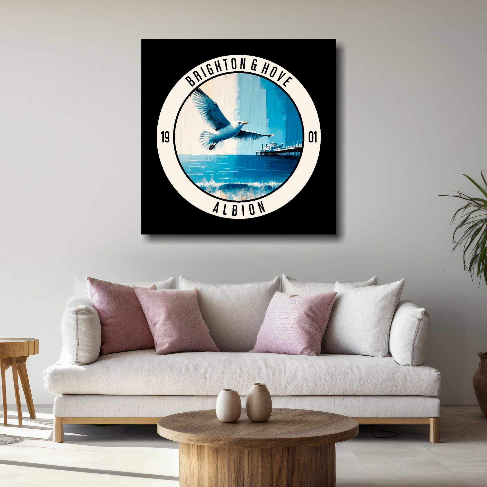 Brighton FC inspired canvas, featuring a large seagull, beach and pier on black background. Mounted on a grey wall above a white sofa with decorative cushions.