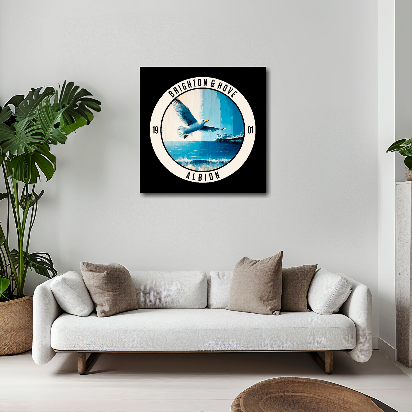 20 inch by 20 inch Brighton FC inspired canvas, featuring a large seagull, beach and pier on black background. Mounted on a white wall above a white sofa with decorative cushions.