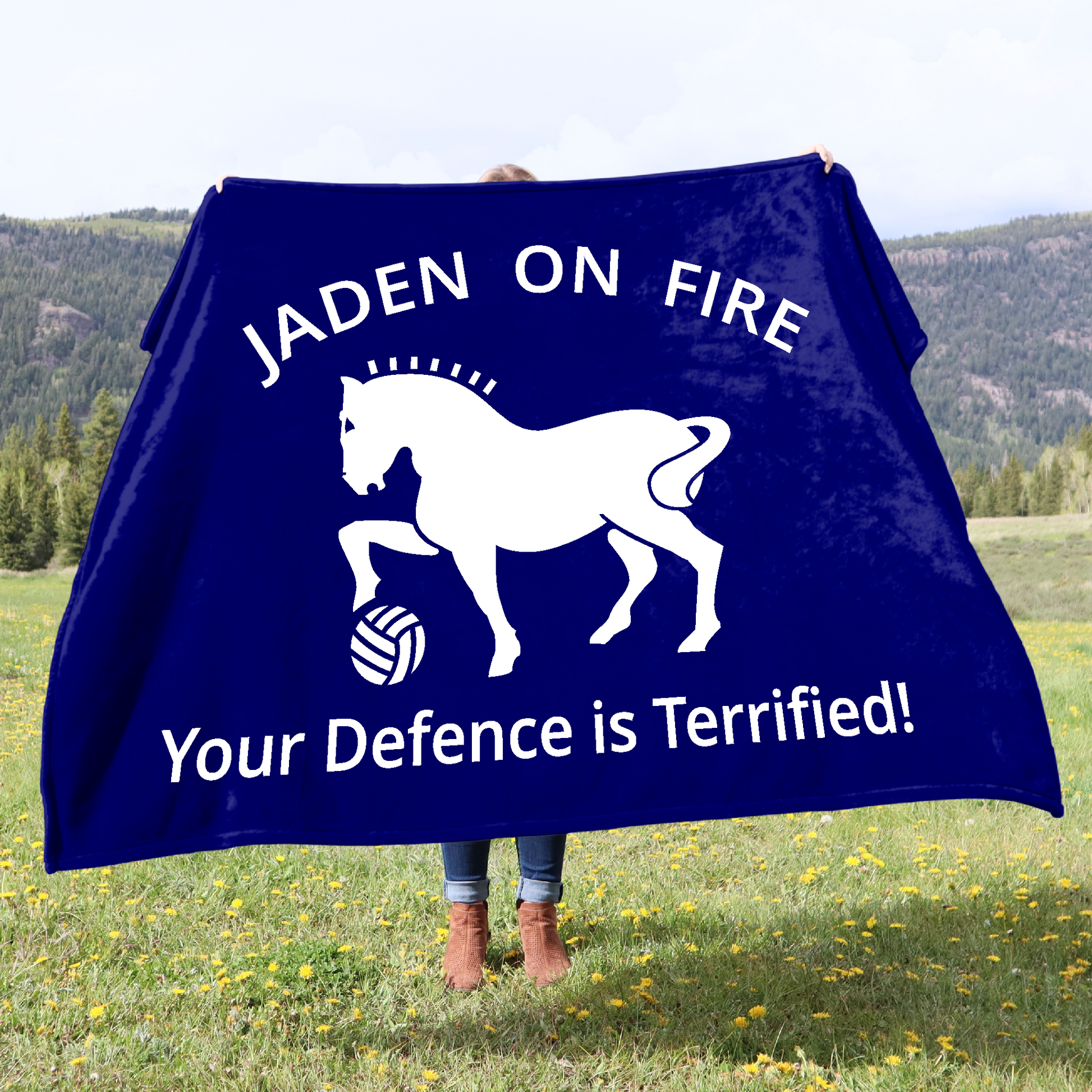 A woman holding a blue blanket, personalised with white text and horse graphic in a field.